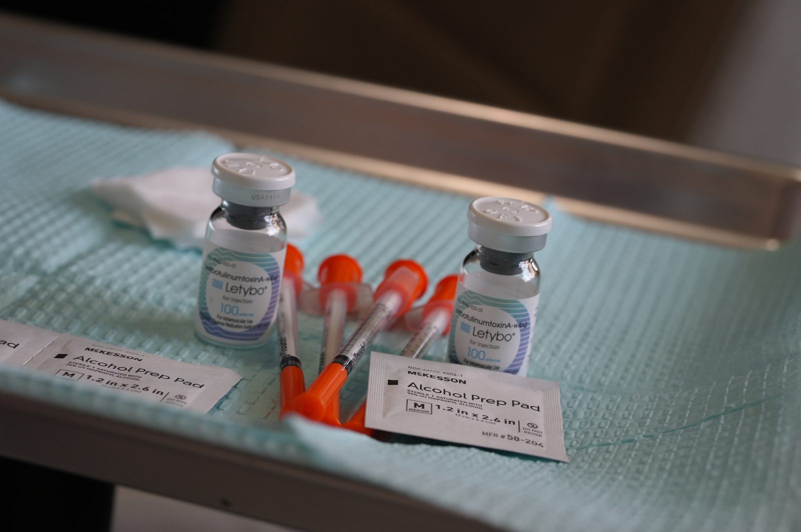 Two Letybo 100 Units vials, four orange-capped syringes, two McKesson alcohol prep pads and a gauze square on a teal drape in a steel tray