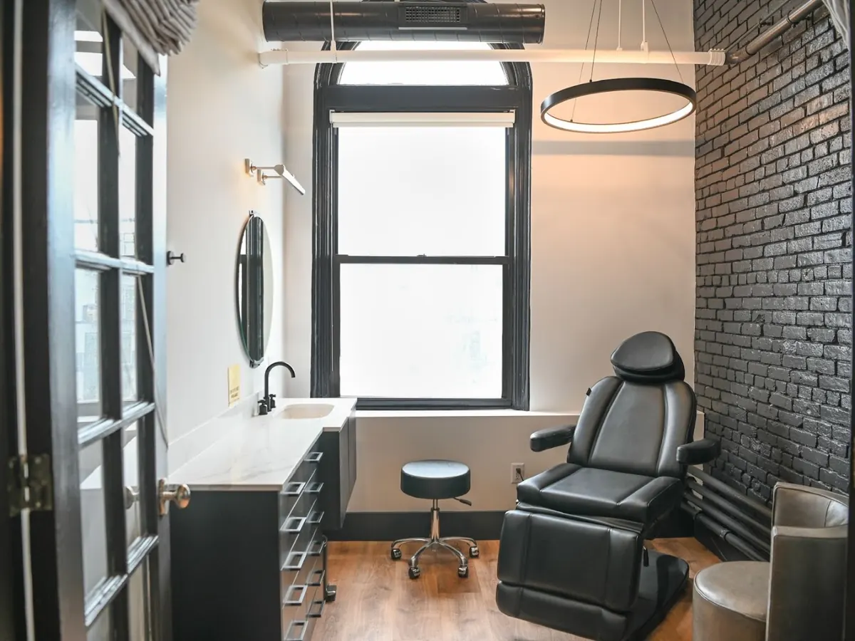 Treatment room with black reclining chair, dark vanity, ring pendant light and black brick wall