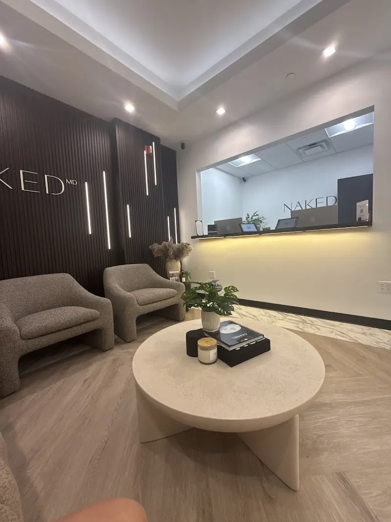 Waiting area with grey armchairs and a round table beneath NAKED MD lettering on a slatted wall
