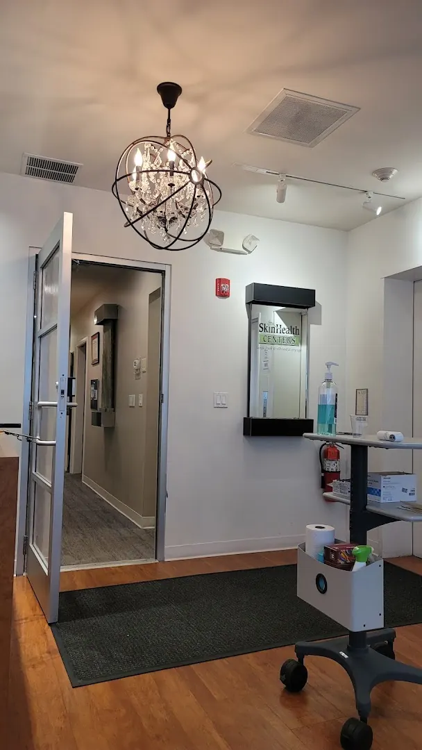 Suite entrance with a SkinHealth Centers wall sign, orb chandelier and open glass door
