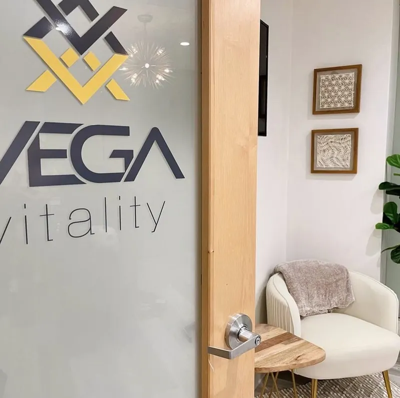 Frosted glass door with a large VEGA vitality logo beside a cream armchair and framed art