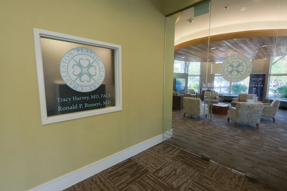Wall sign with Charleston Plastic Surgery seal and two surgeon names beside a glass door