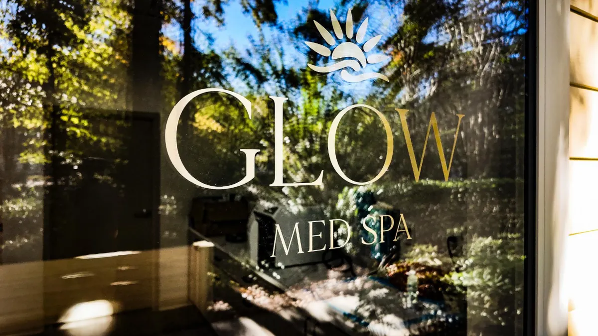 Window glass with GLOW MED SPA lettering and a sun logo, trees reflected
