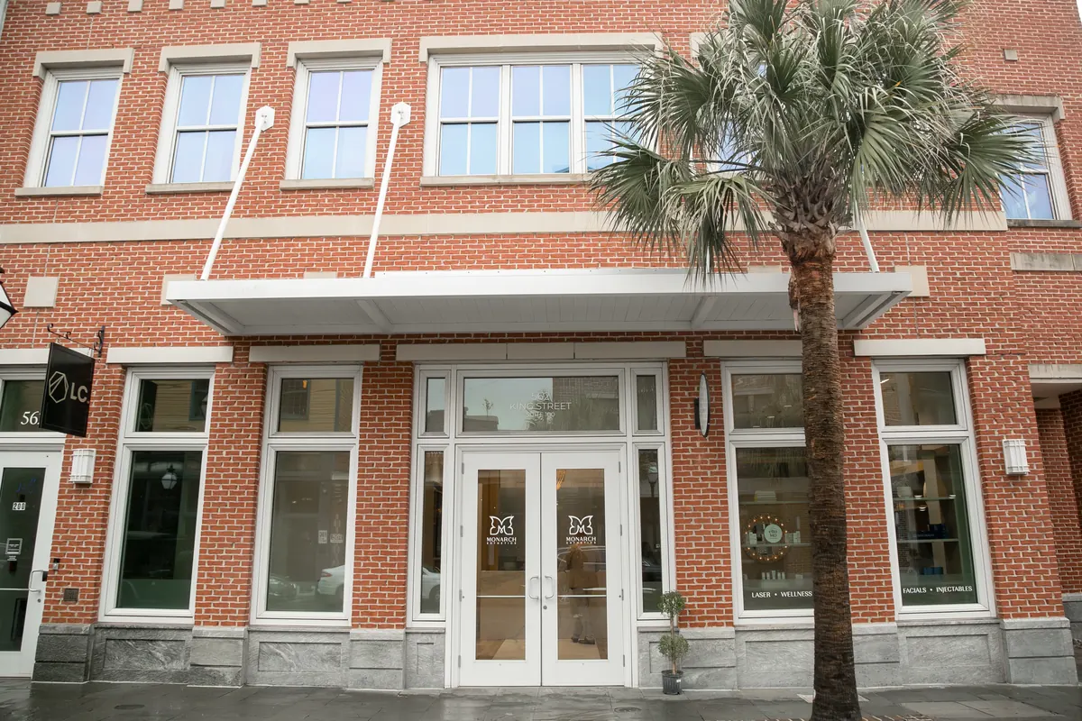 Red brick storefront with white double glass doors and a palm tree