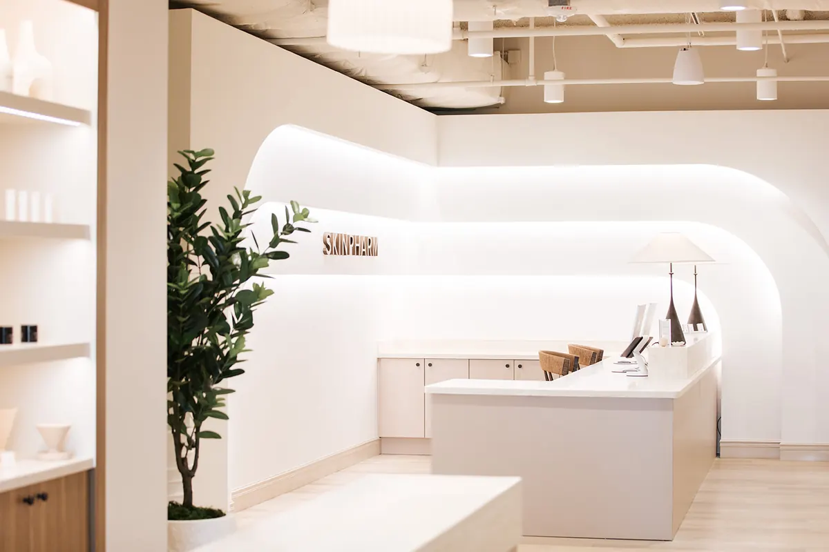 White curved reception desk with a SKINPHARM wall sign and pendant lights