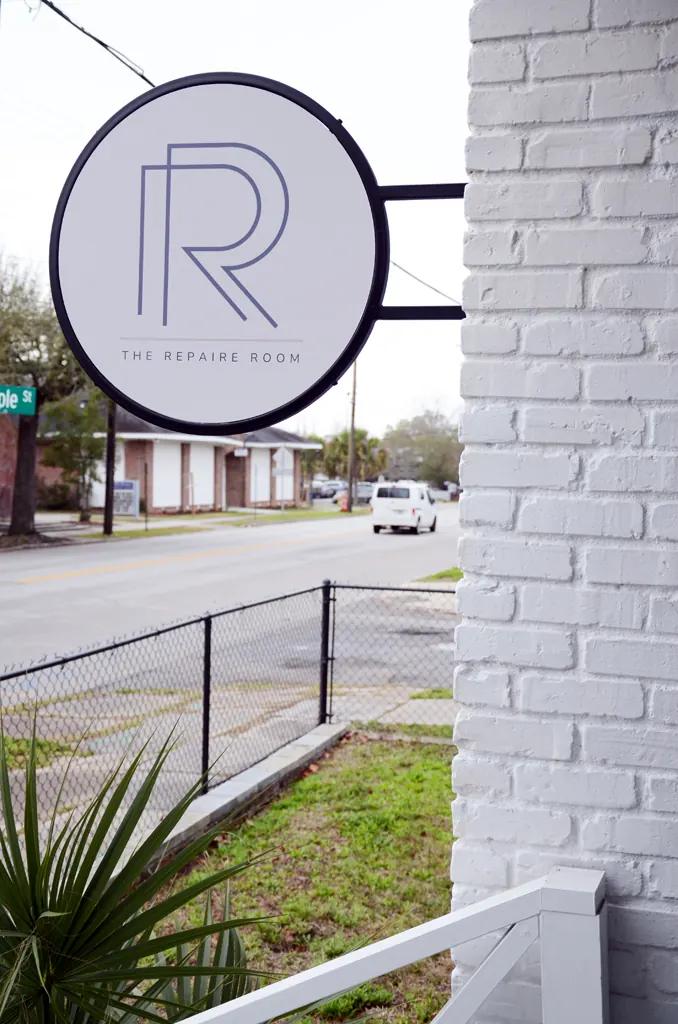 Round hanging sign reading The Repaire Room on a white painted brick wall