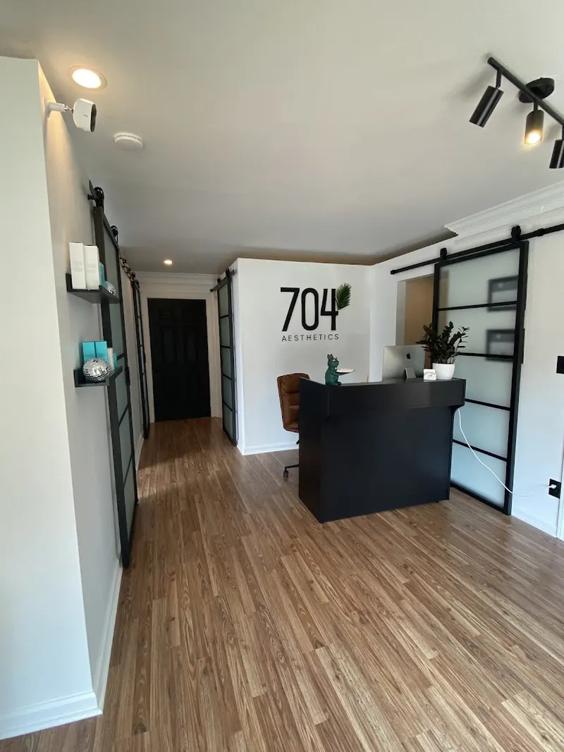 Black reception desk below a 704 Aesthetics wall logo, with frosted barn doors