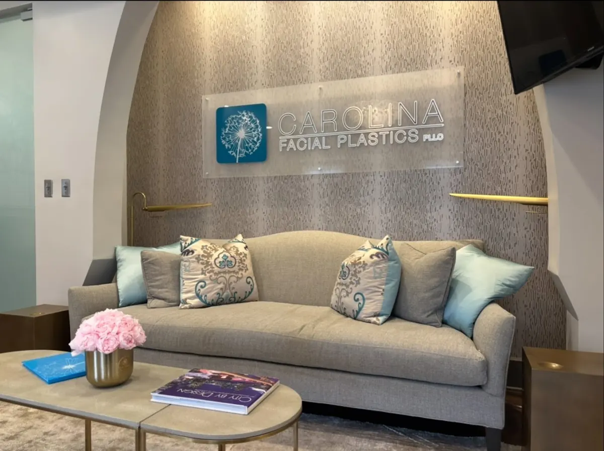Grey sofa with teal pillows beneath a frosted Carolina Facial Plastics wall sign