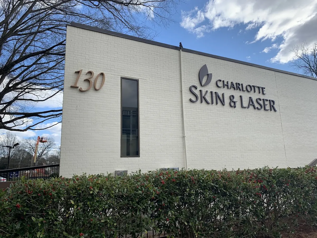 White brick building with a bronze 130 and Charlotte Skin & Laser lettering above a hedge