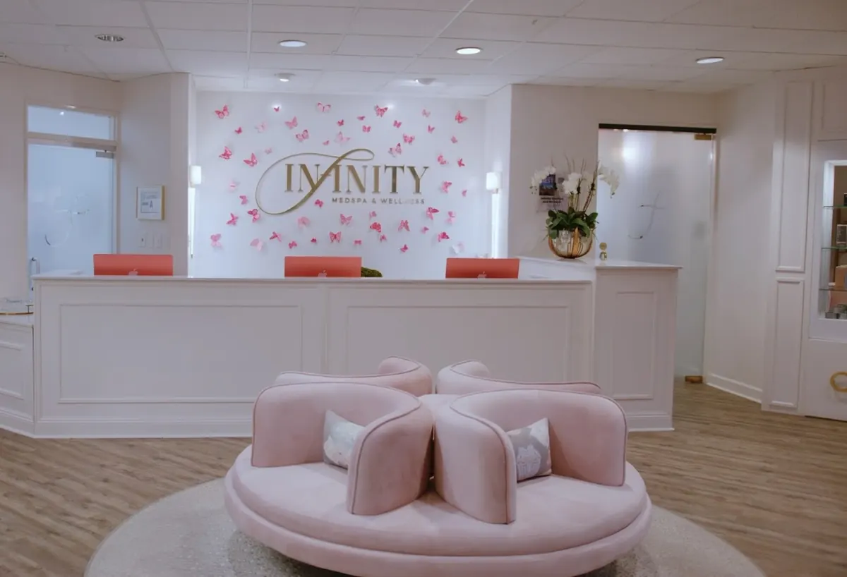 Reception desk with gold Infinity MedSpa & Wellness wall sign, pink butterflies and round pink sofa