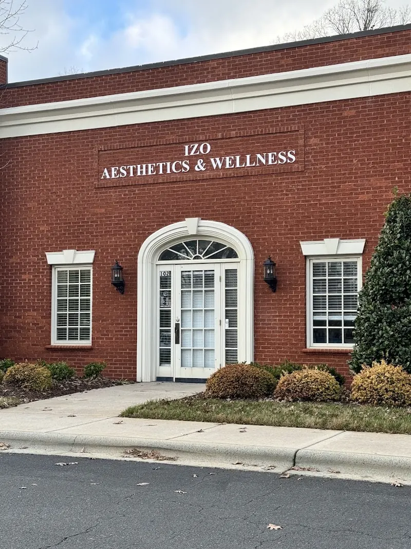 Red brick building with IZO Aesthetics & Wellness lettering above an arched white entry door