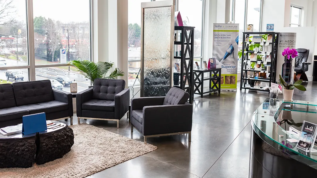 Waiting lounge with charcoal armchairs, a water wall and Jon'Ric displays on the reception counter