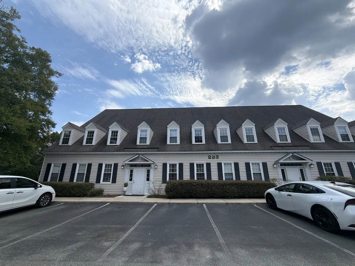 Two-storey building with dormers and black shutters, the number 233 above the entrance and a parking lot