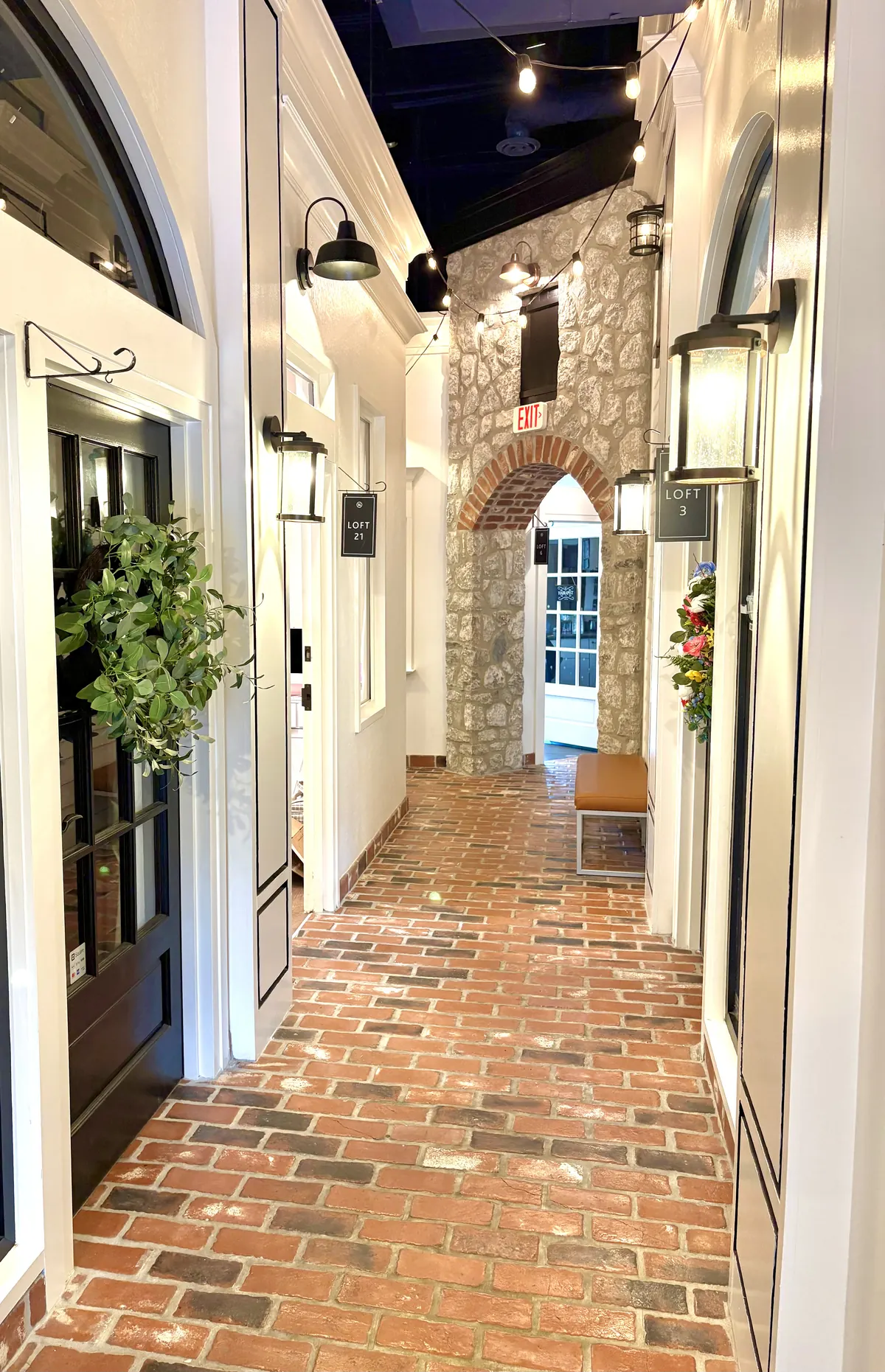 Brick-floored corridor with white doors, wall lanterns and a hanging Loft 21 sign