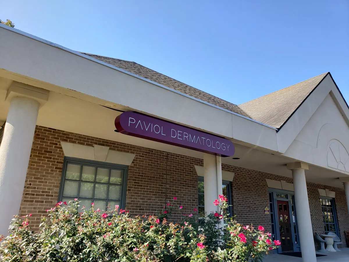 Brick office entrance with white columns and a purple Paviol Dermatology sign under the eave