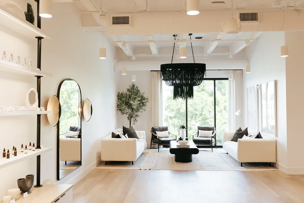 Lounge with cream sofas, leather armchairs and a black fringe chandelier beside product shelves