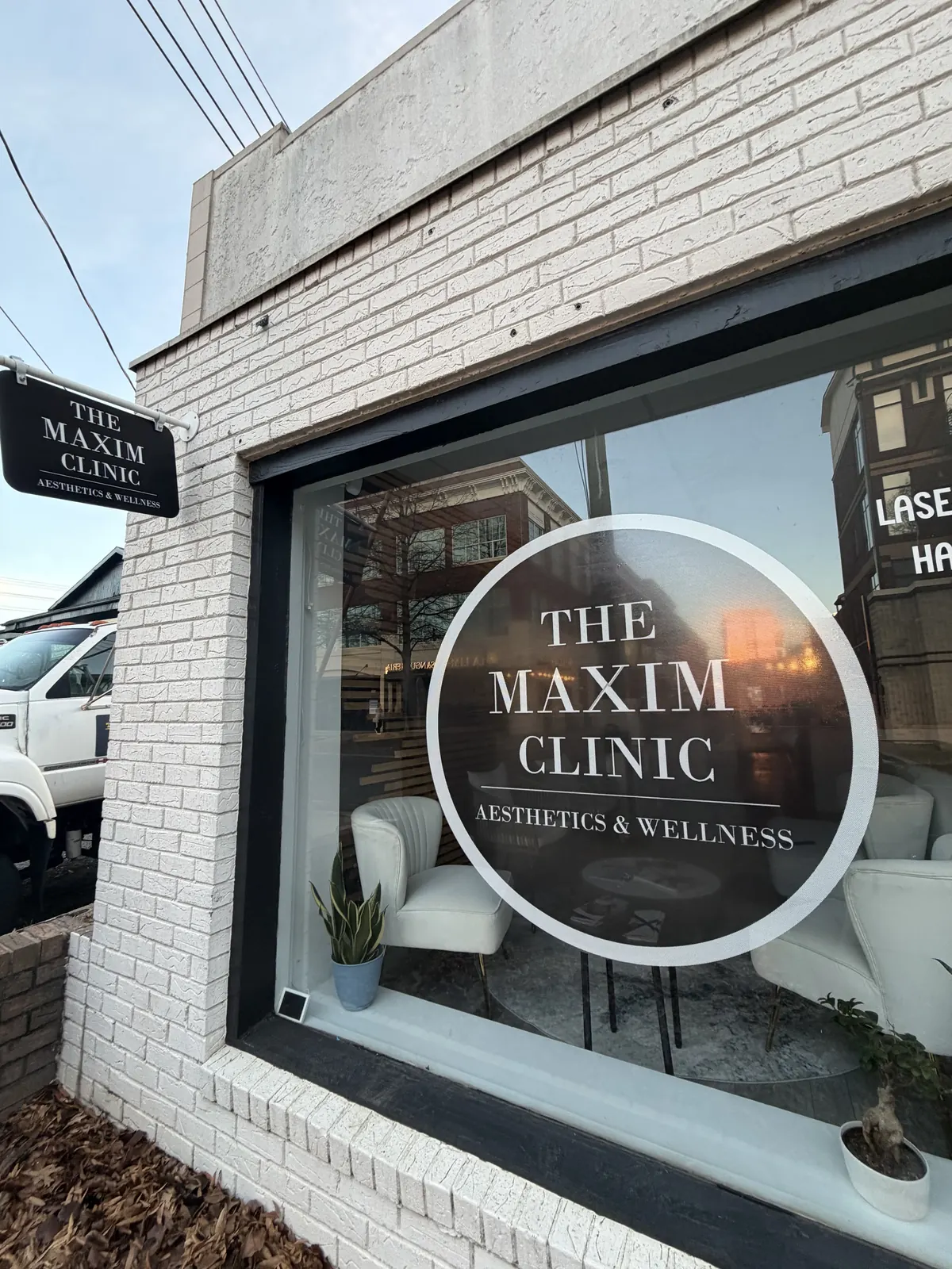 White brick storefront with a round window logo reading The Maxim Clinic Aesthetics & Wellness