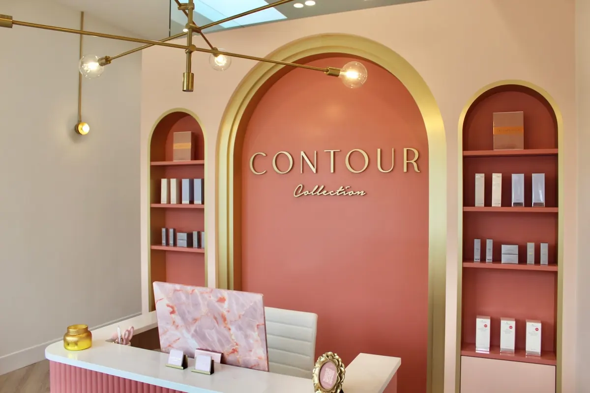 Reception desk before a coral arch with gold CONTOUR Collection lettering and product shelves