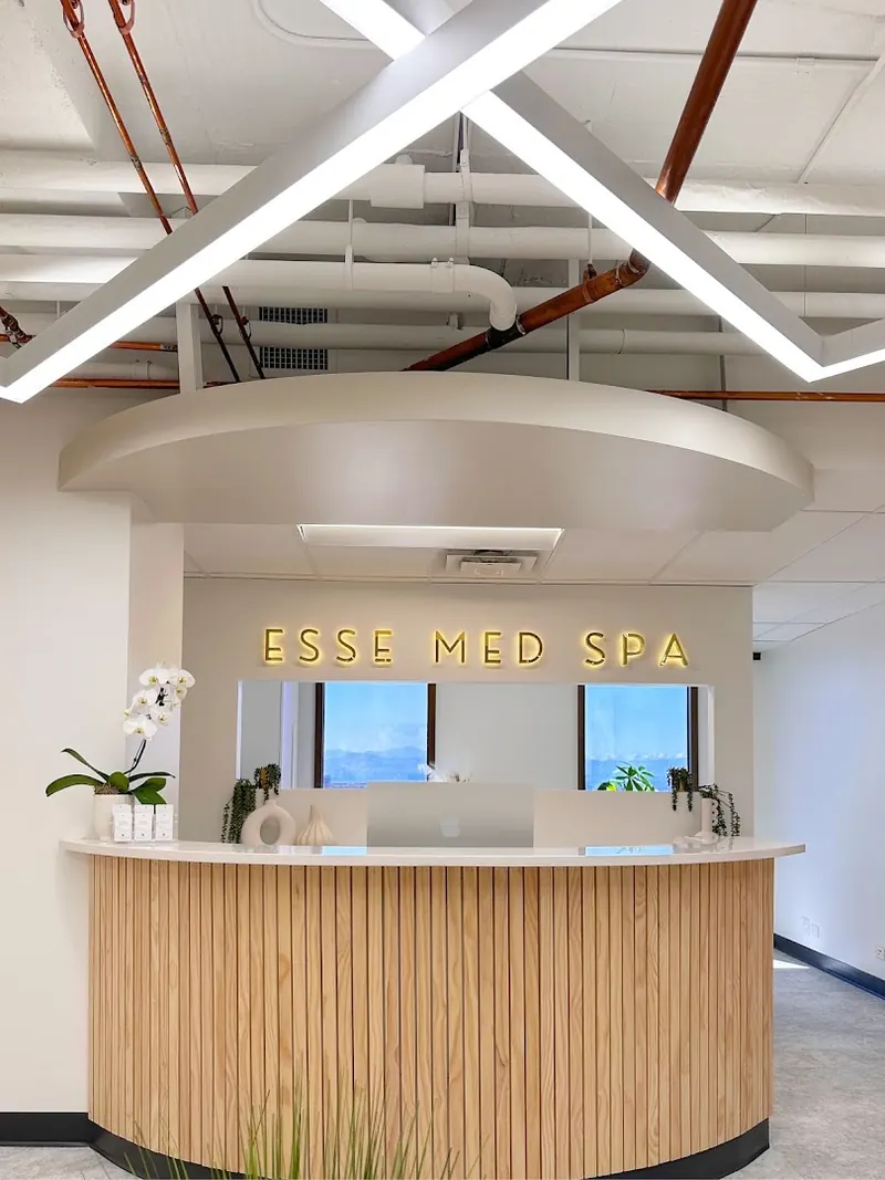 Curved slatted-wood reception desk beneath illuminated ESSE MED SPA letters