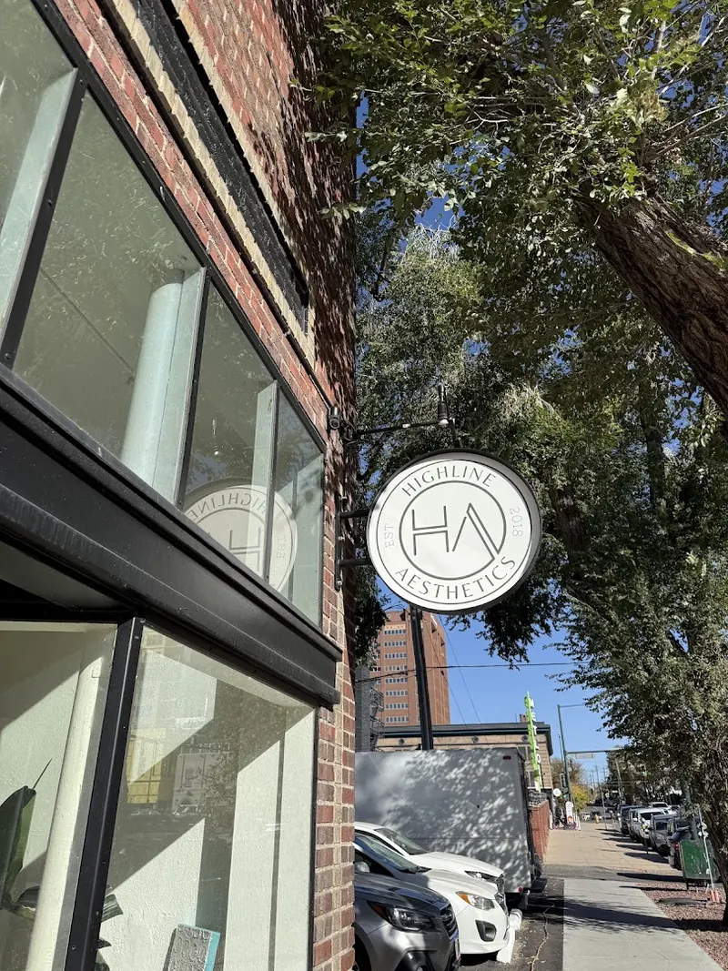 Round Highline Aesthetics blade sign hanging from a brick storefront under trees