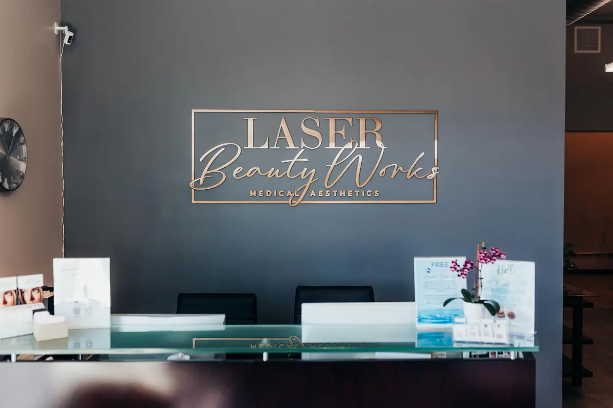 Glass reception counter beneath a rose-gold Laser Beauty Works Medical Aesthetics wall sign
