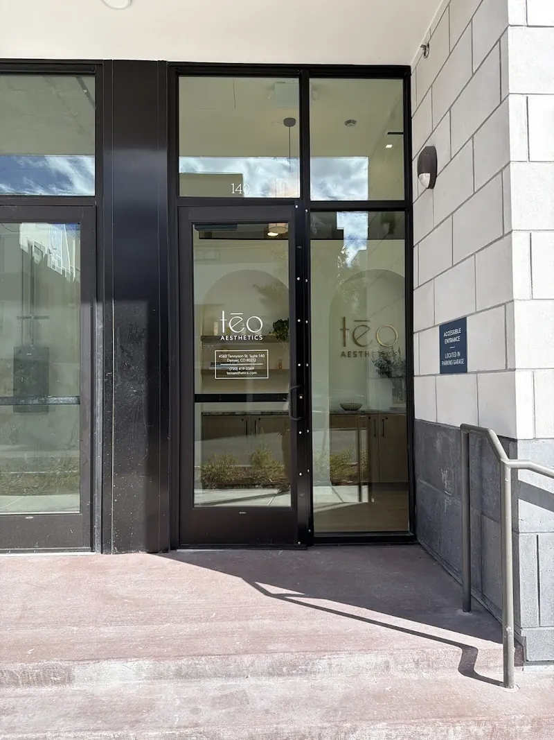 Black-framed glass entrance with a Teo Aesthetics door decal and a handrail
