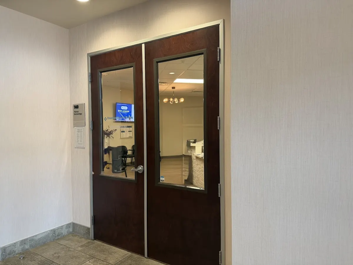 Wood double doors with windows beside a suite 140 Thomas Dermatology wall plaque