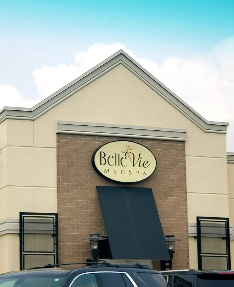 Oval Belle Vie MedSpa sign above a dark awning on a tan gabled building