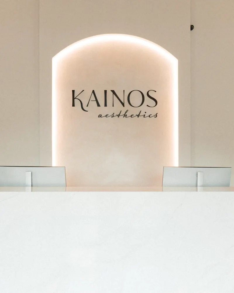 Kainos Aesthetics logo in a backlit arch behind a white marble reception counter