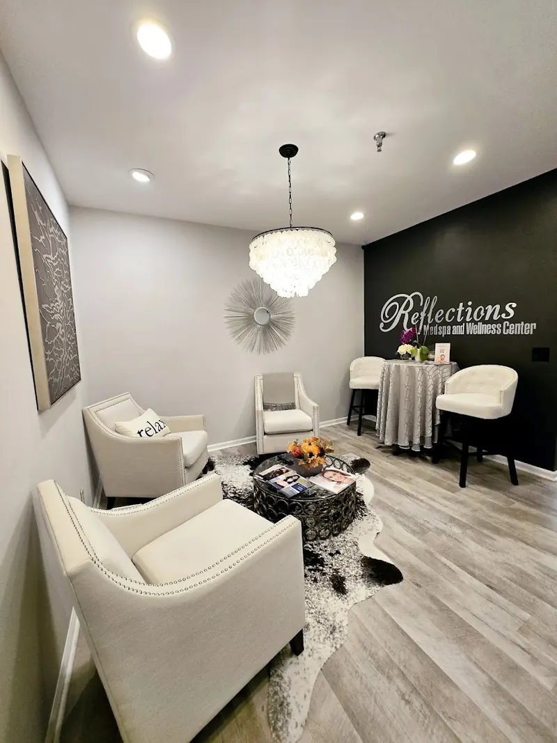 Lounge with cream armchairs, shell chandelier and Reflections Medspa and Wellness Center wall lettering