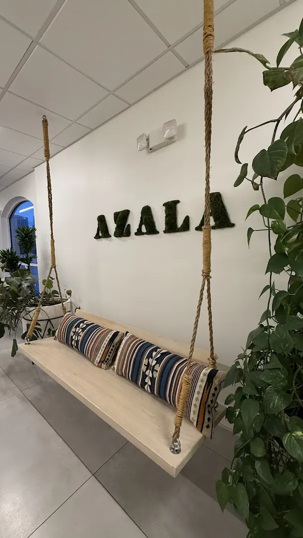 Rope-hung wooden swing bench with patterned pillows below green moss AZALA wall letters