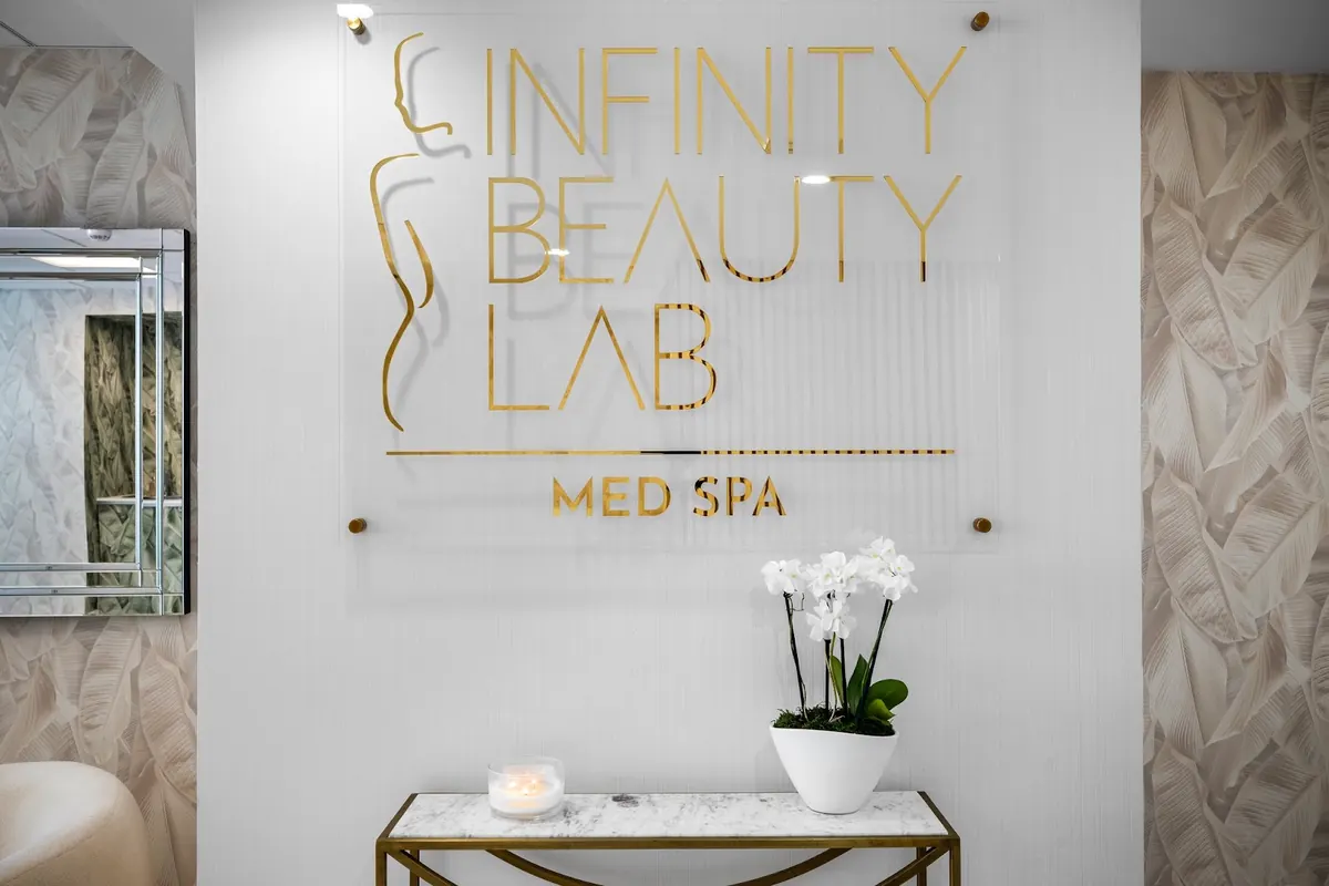 Gold Infinity Beauty Lab Med Spa wall sign above a marble console table with orchids