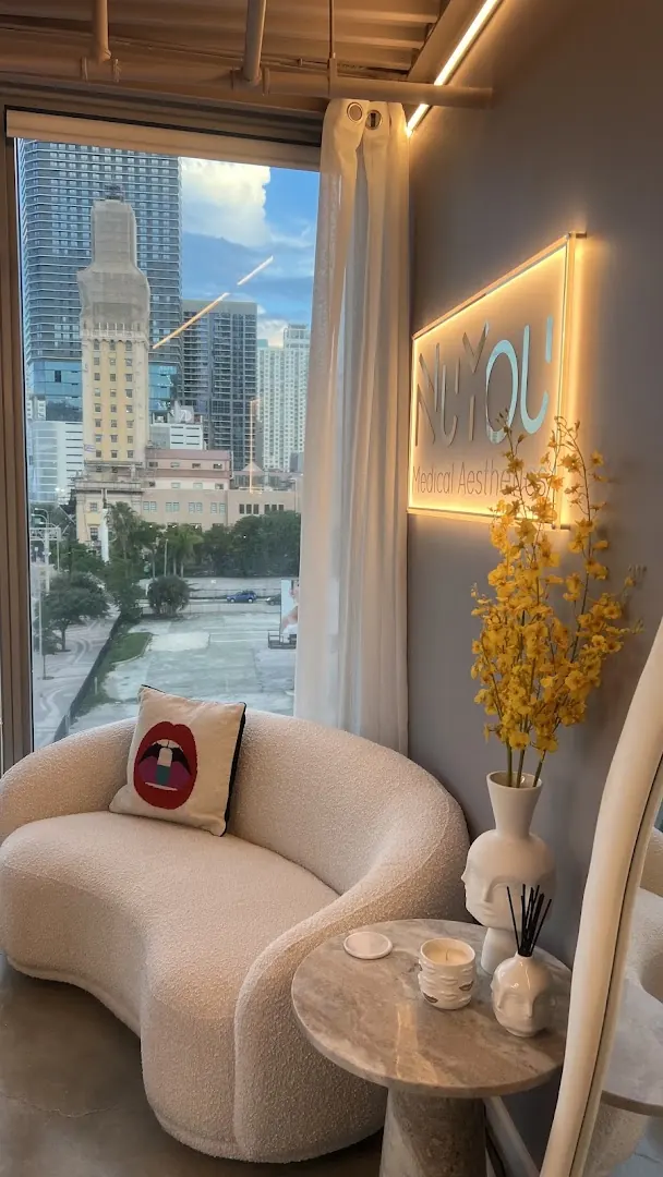 Boucle loveseat beside a city-view window under a backlit NuYou Medical Aesthetics sign