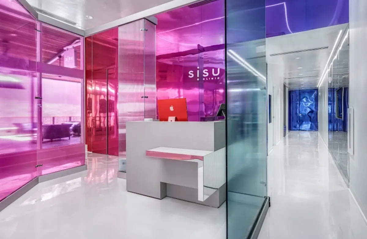 Reception desk with a red computer against magenta glass walls beneath a Sisu Clinic sign