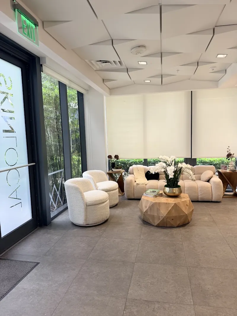 Waiting lounge with cream boucle chairs, a sofa and faceted wood table by tall windows