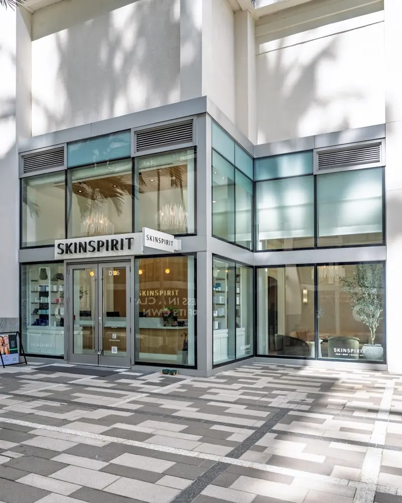 SkinSpirit corner storefront with glass walls on a patterned paver plaza