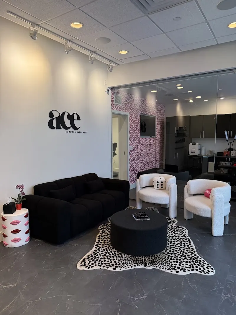 Waiting lounge with black sofa, white armchairs and an ace Beauty & Wellness wall logo