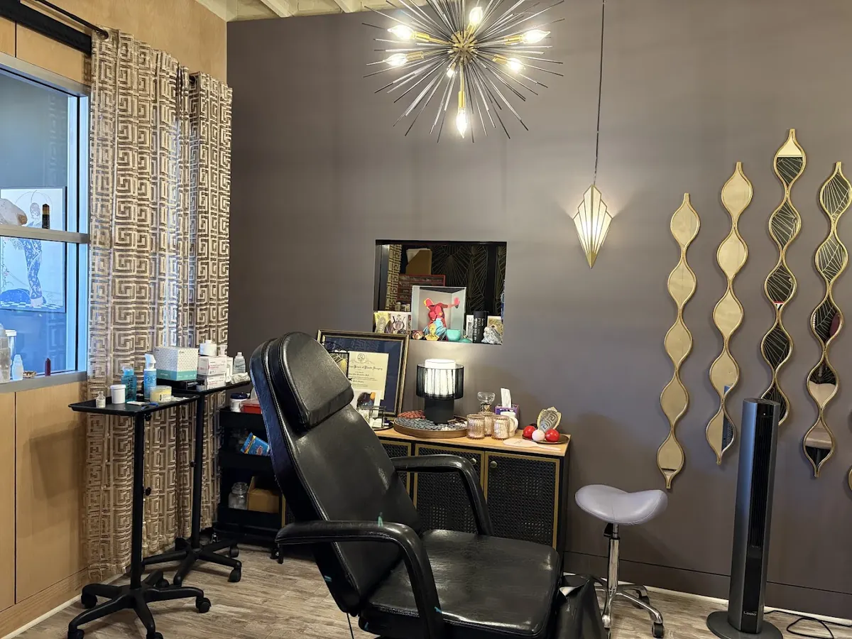 Treatment room with black reclining chair, starburst chandelier and wavy gold-framed mirrors