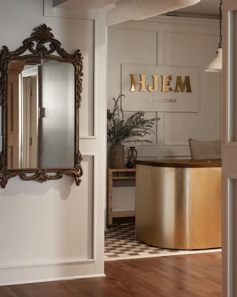 Gold Hjem Aesthetics wall sign above a curved gold reception desk, beside an ornate mirror