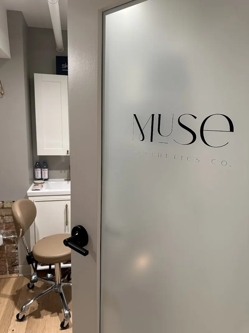 Frosted treatment room door with Muse Aesthetics Co. logo, opening onto a stool and sink