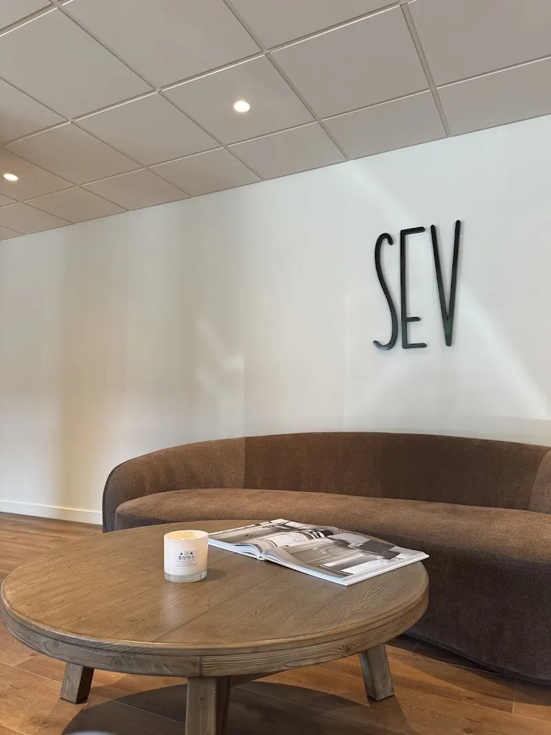 Waiting lounge with brown curved sofa, round wooden table and black SEV wall letters