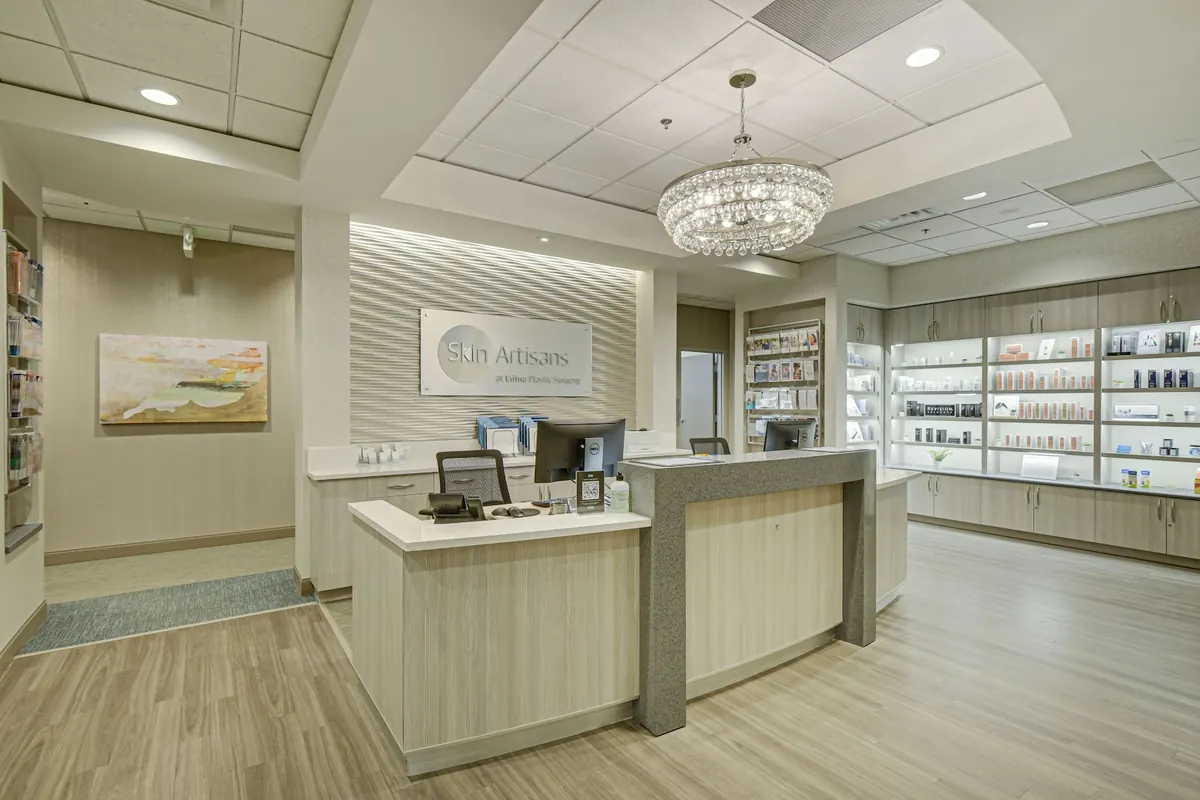 Reception desk under a crystal chandelier with a Skin Artisans at Edina Plastic Surgery sign
