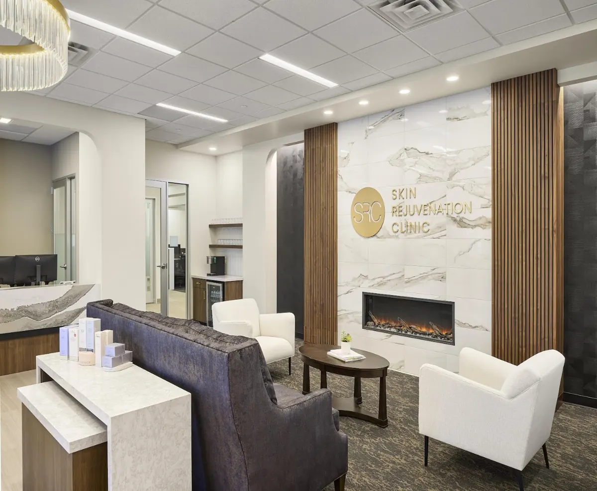 Lounge with white armchairs and a fireplace below a gold Skin Rejuvenation Clinic wall sign
