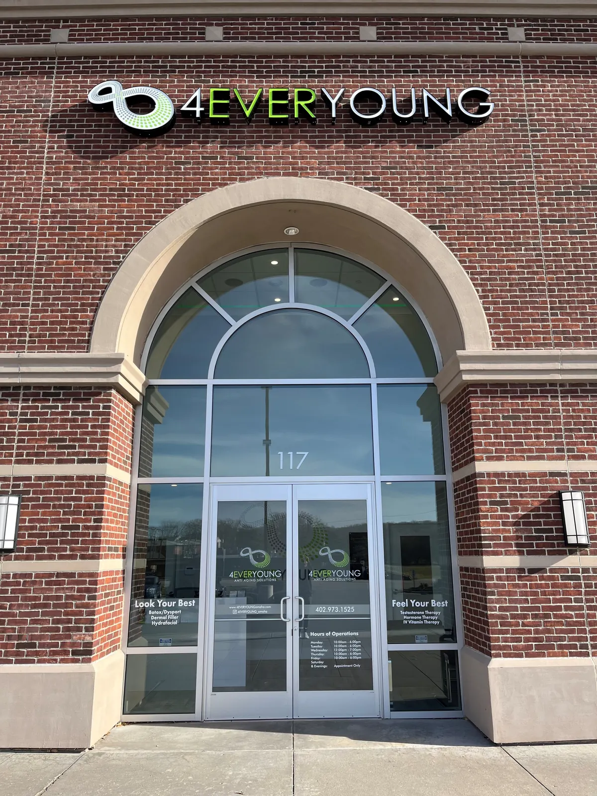 Brick entrance arch with 4EVERYOUNG lettering and glass doors carrying logo and hours