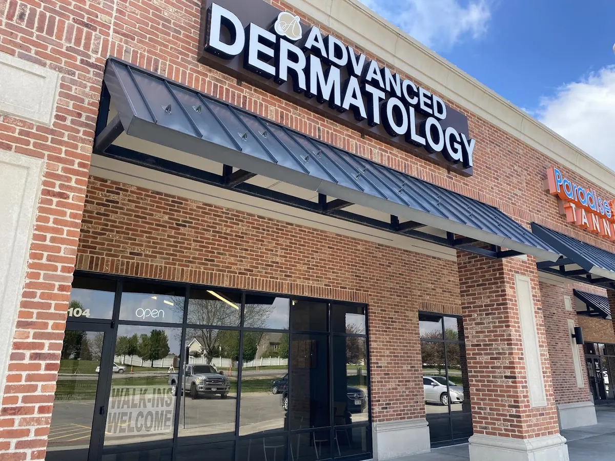Brick storefront with lit Advanced Dermatology sign, metal awning and suite 104 on the door