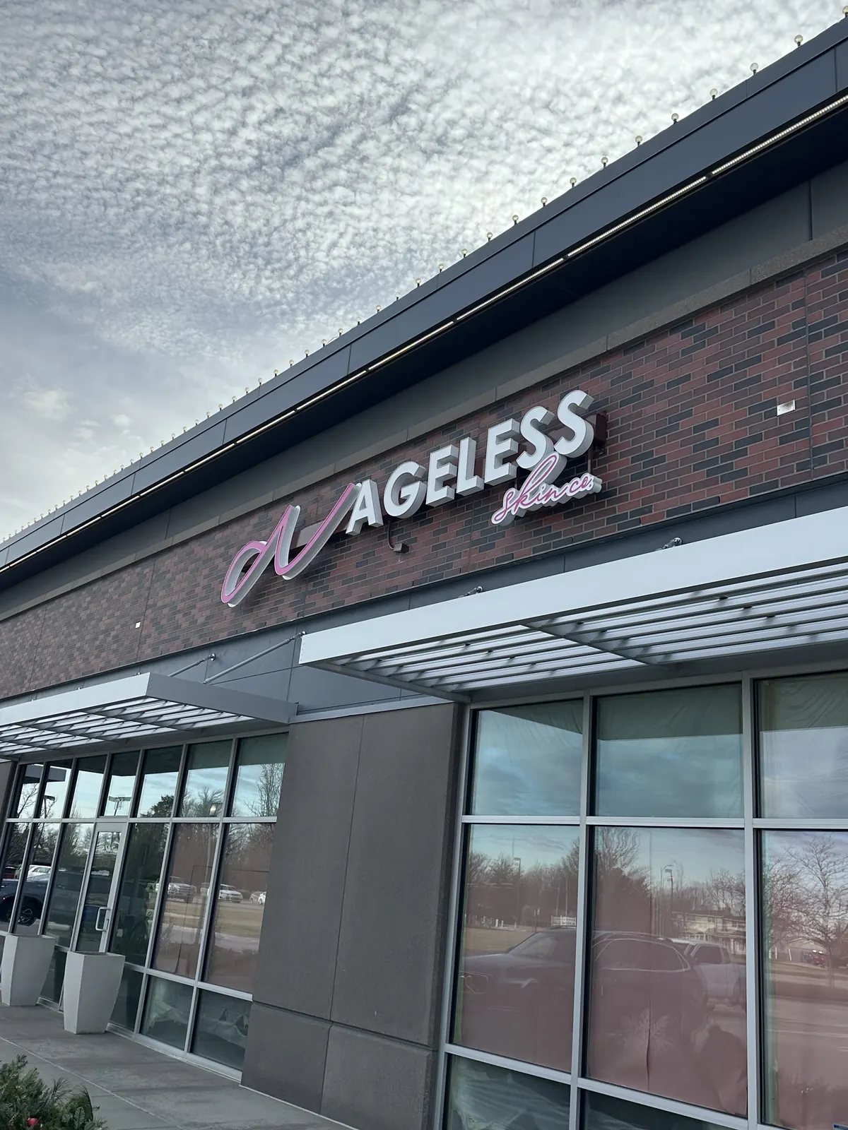 Storefront with a lit Ageless logo sign on a brick and glass building