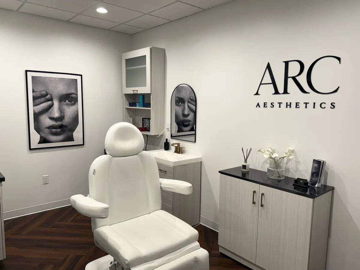 White treatment chair and cabinet beside a black ARC Aesthetics wall logo