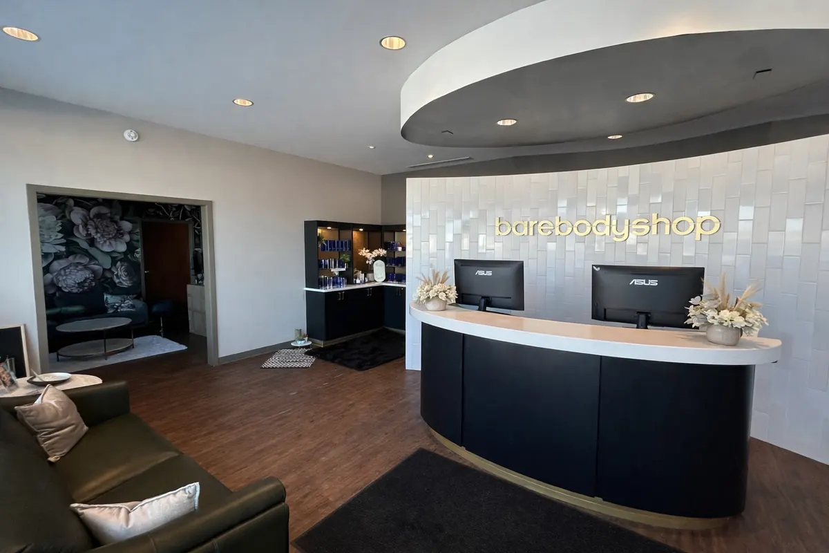Curved reception counter under gold barebodyshop lettering on a tiled wall