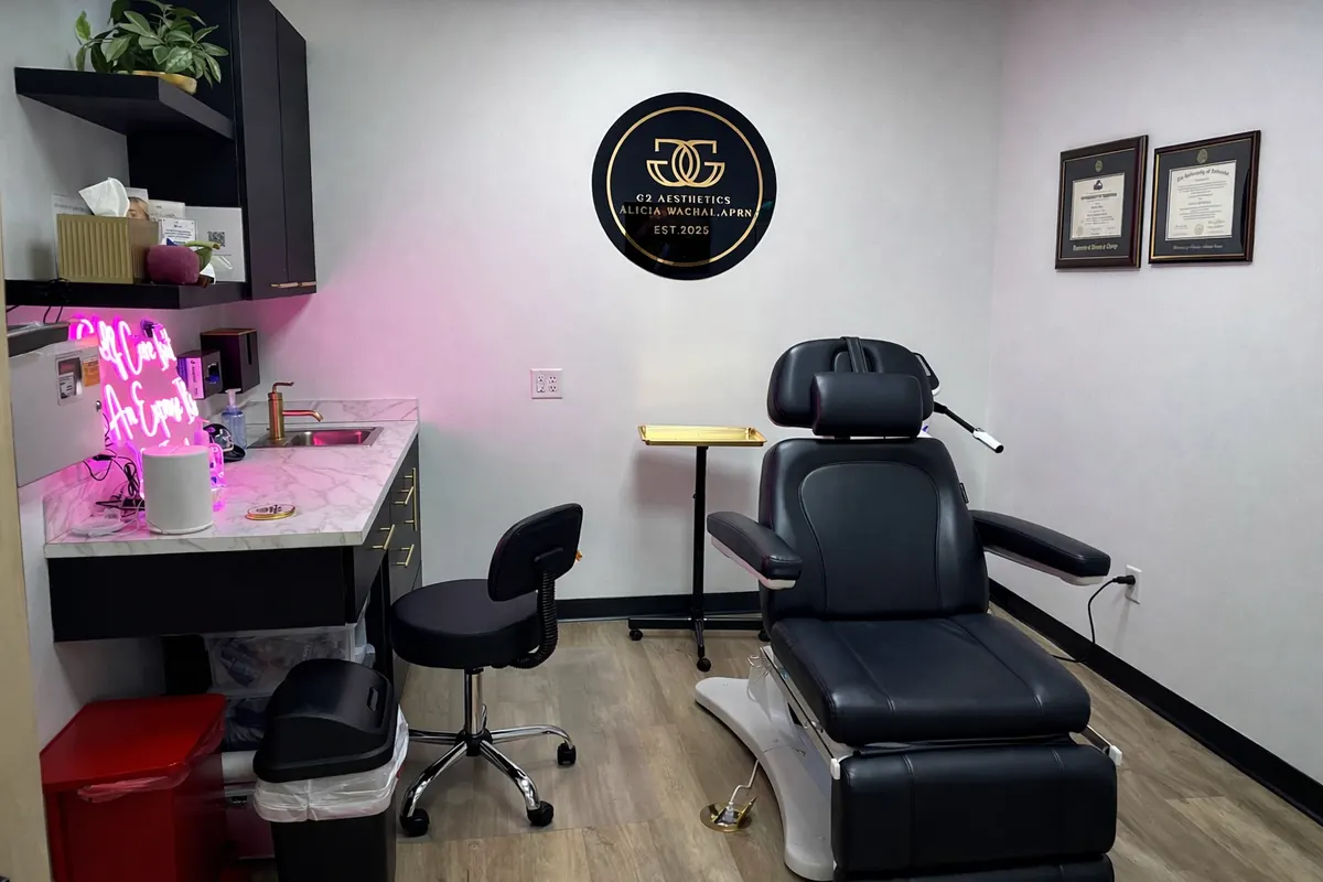 Black treatment chair and stool beneath a round gold G2 Aesthetics wall logo