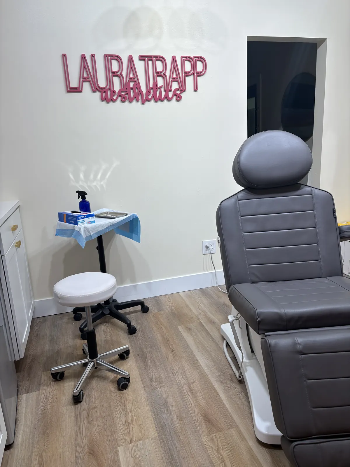 Black treatment chair and stool below pink Laura Trapp Aesthetics wall lettering